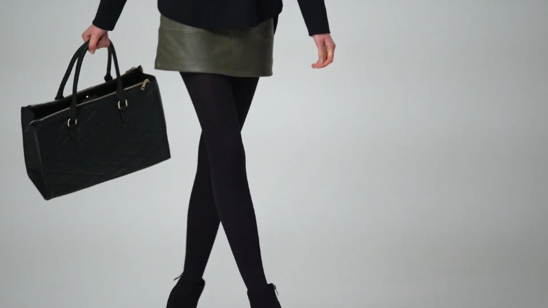 Žena u kožnoj mini suknji i crnim hulahopkama nosi crnu torbu, uz elegantne cipele na štiklu