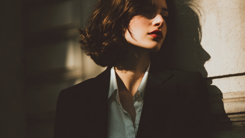 Žena u crnom blejzeru i beloj košulji stoji uz zid