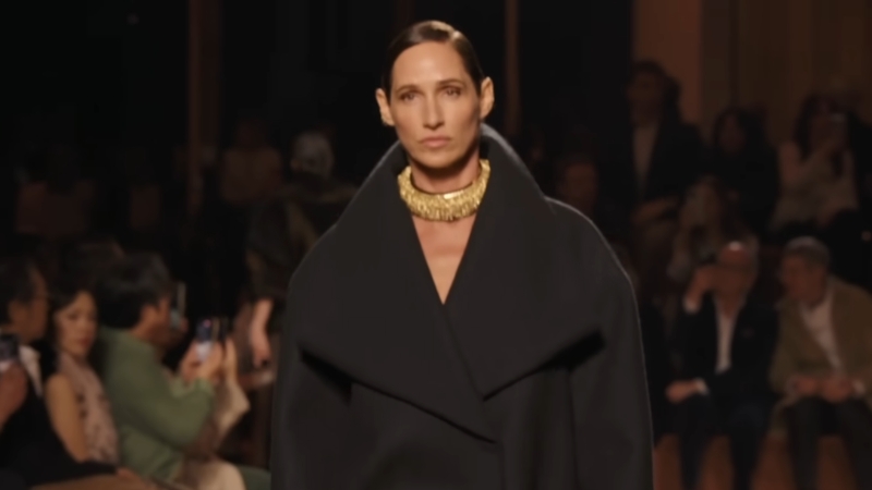 Model nosi tamnu elegantnu kreaciju sa naglašenim okovratnikom na pisti tokom Milanske nedelje mode 2025