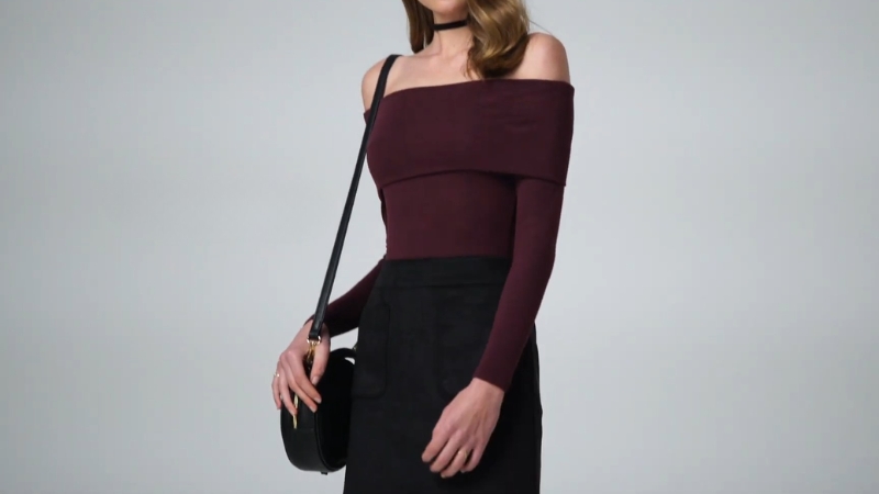 Žena u crnoj mini suknji i bordo topu sa spuštenim ramenima nosi malu crnu torbu na ramenu